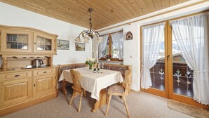 A cozy dining area with wooden furniture, a chandelier, and a view through a glass door. - Ferienwohnung Kaiserstüberl (Reit im Winkl)
