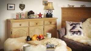 A cozy living room with a wooden cabinet, a fluffy white throw on a sofa, a table with a mug, apples, and a card. - Ferienwohnung Kaiserstüberl (Reit im Winkl)