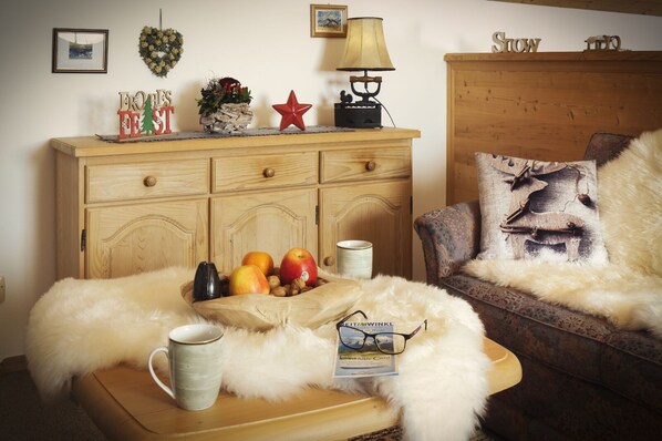 A cozy living room with a wooden cabinet, a plush sofa, a coffee table with a mug, apples, and a card.