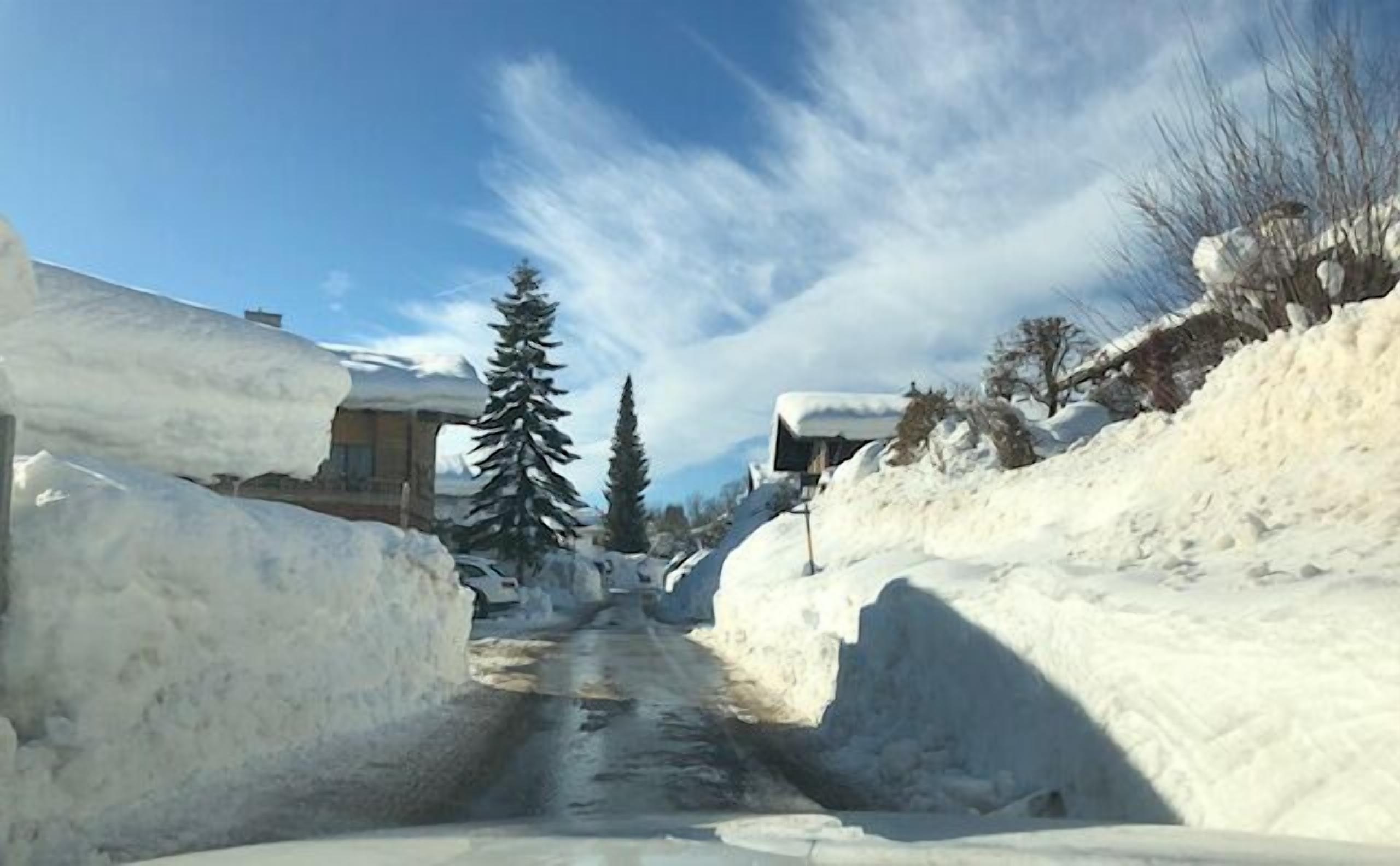 A narrow snow-covered road flanked by buildings and trees.