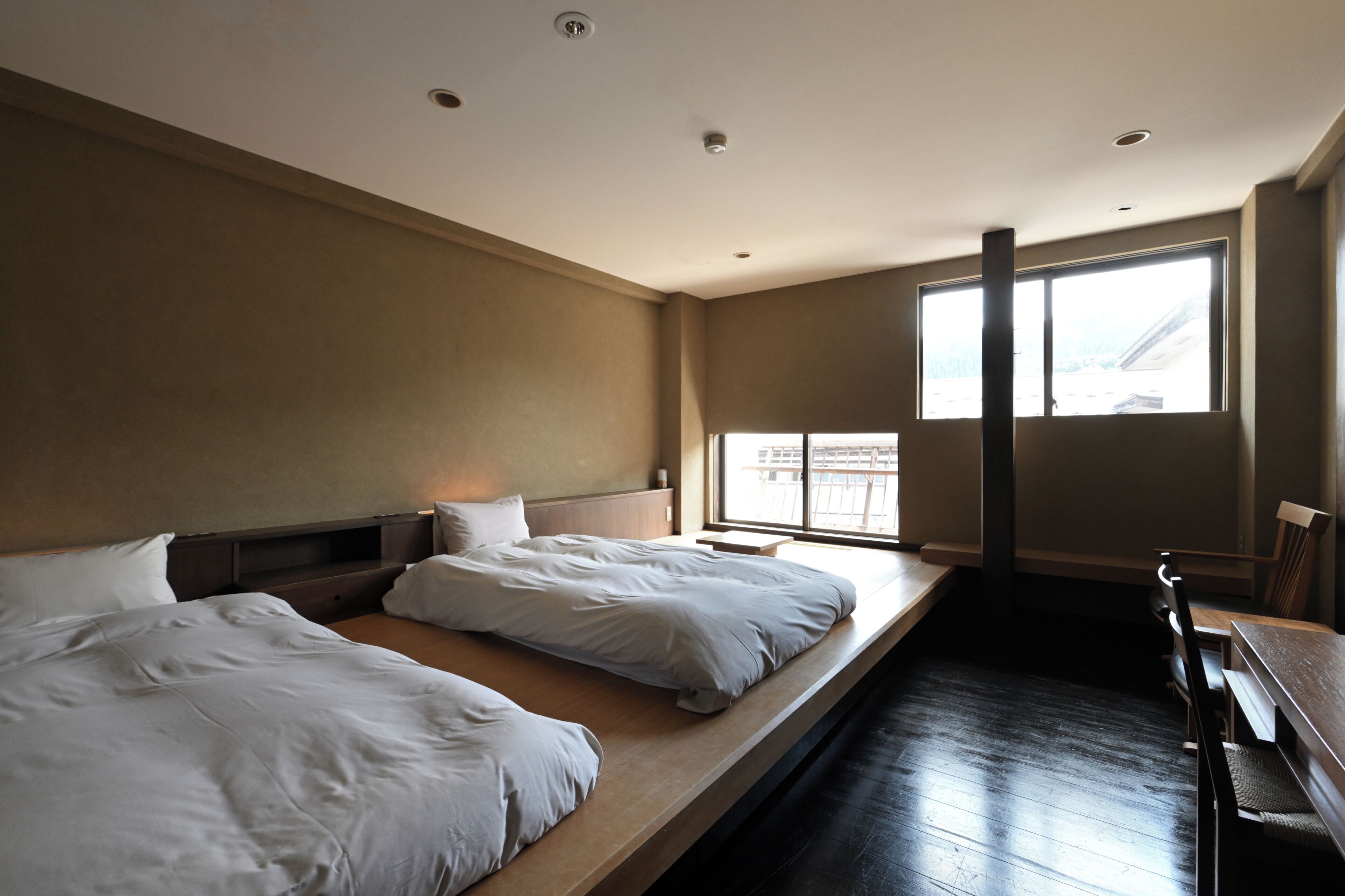 A hotel room with two beds, a large window, and a wooden bench.