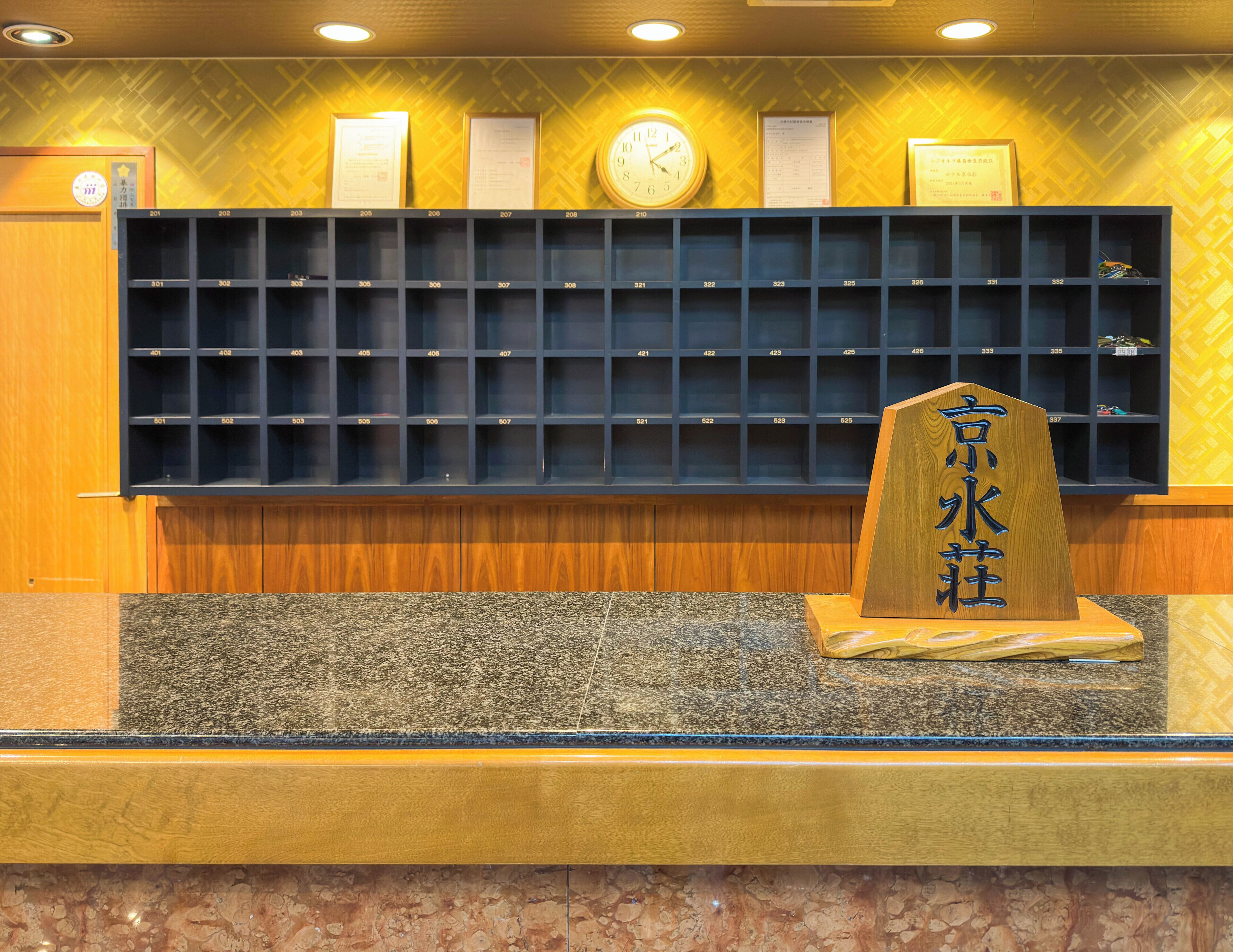 A reception desk with a clock, framed certificates, and a wooden sign with Chinese characters.