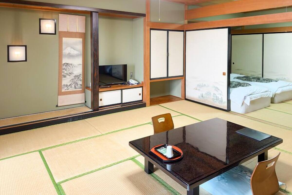 Une pièce de style japonais traditionnel, avec un sol recouvert de tatamis, une petite table basse avec un plateau et un lit doté d’une literie de type futon.