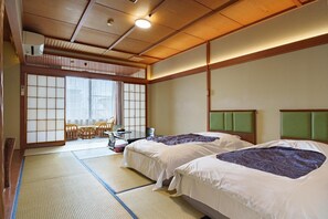 A traditional Japanese-style room with tatami flooring, two beds with green headboards, a sliding shoji screen door, and a view of a garden.