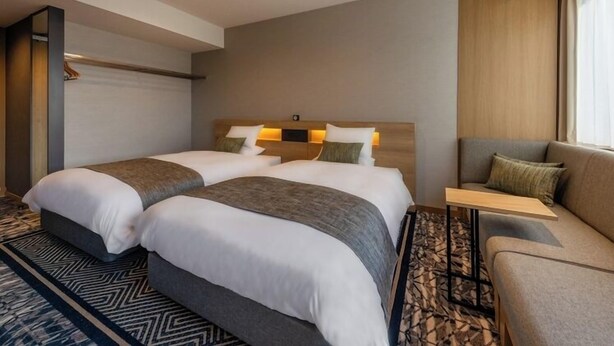 A hotel room with two beds, a sofa, a small table, and a large window. - TAS Park Hotel Nagai (Nagai)