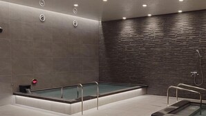 A modern spa with a rectangular hot tub, a separate smaller hot tub, and a shower area. - TAS Park Hotel Nagai (Nagai)