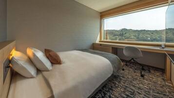 Una habitación de hotel con cama, escritorio y ventana con vista a un área boscosa.