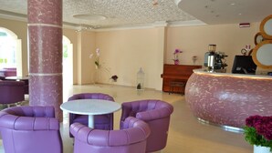 A lobby with purple seating, a reception desk, and a coffee machine. - Hotel Castellucci (Bellaria-Igea Marina)