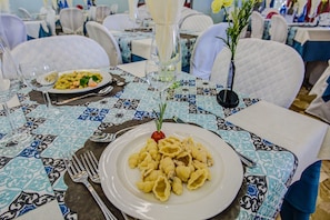 Una mesa de comedor con un plato de pasta, un vaso de agua y un florero con flores.