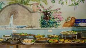 A buffet with various dishes and a mural with tropical plants and a fountain. - Hotel Castellucci (Bellaria-Igea Marina)