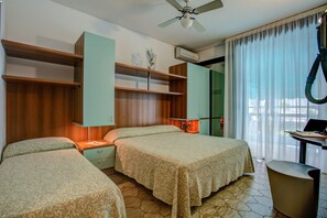Habitación de hotel con dos camas, un escritorio con una computadora portátil, un ventilador de techo y una ventana con cortinas.
