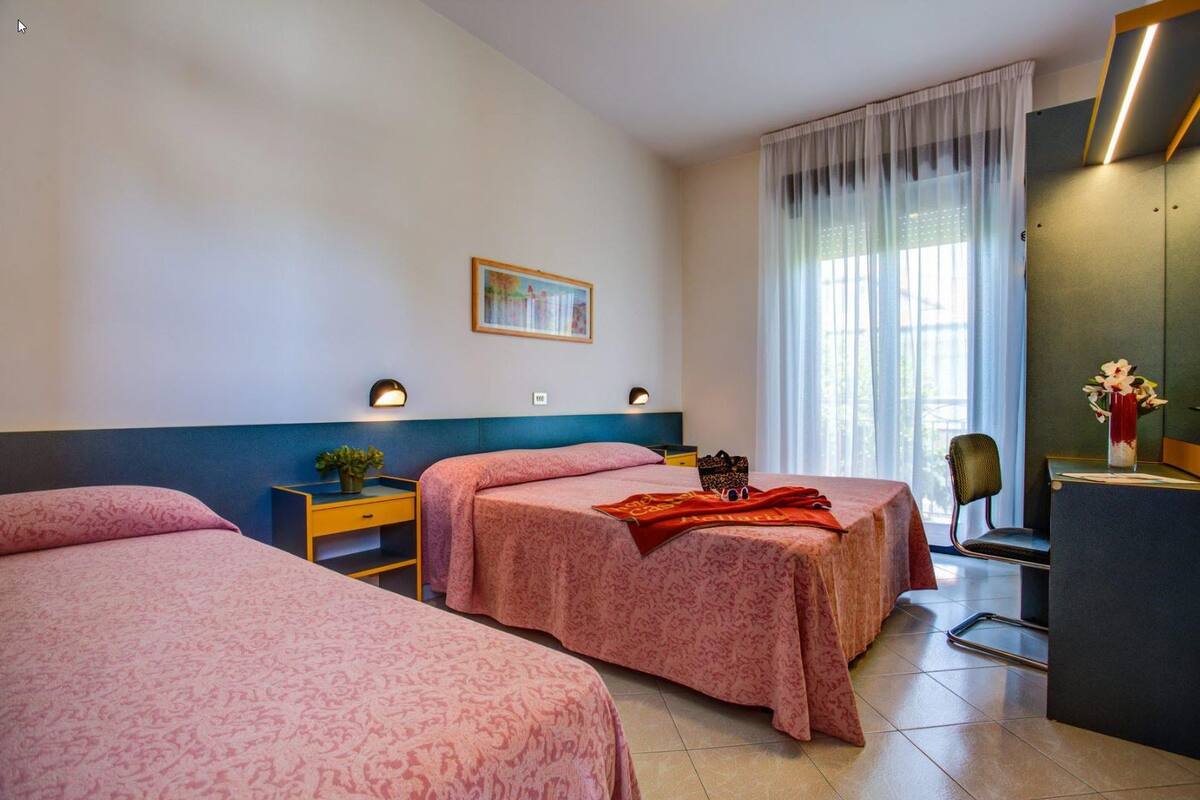 Hotelkamer met twee bedden, een bureau, een stoel, een bureaulamp, een schilderij aan de muur en een raam met gordijnen.