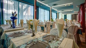 A banquet hall with tables set for dining, featuring a modern ceiling design and large windows with sheer curtains. - Hotel Castellucci (Bellaria-Igea Marina)