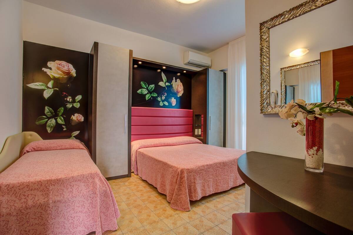 Een hotelkamer met twee bedden, een grote spiegel en een vaas met bloemen op een tafel.