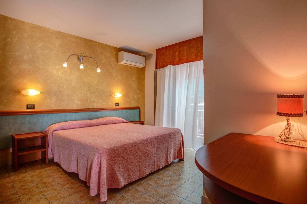 Een hotelkamer met een bed, nachtkastjes, een airconditioner, een lamp en een raam met gordijnen.
