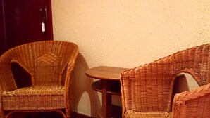 Una habitación con dos sillas de mimbre, una mesita pequeña, una puerta y un espejo en la pared.