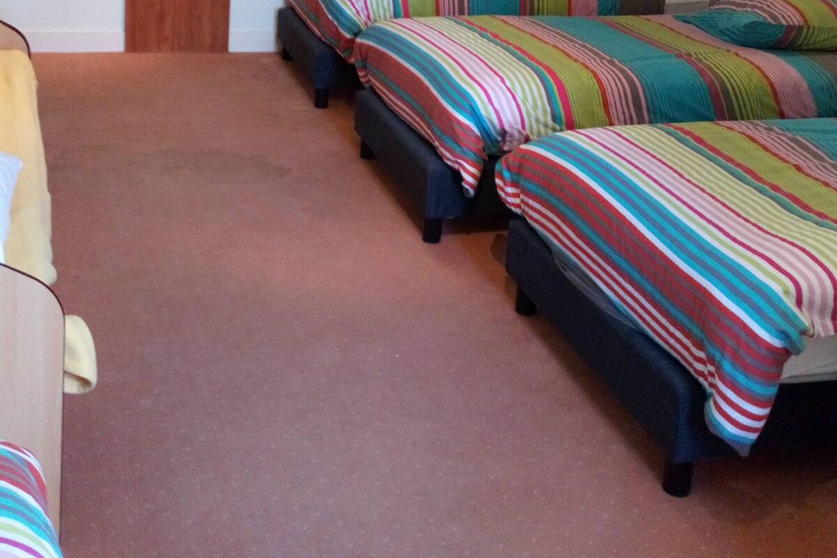 Een kamer met drie bedden, een houten garderobe en een plafondlamp.