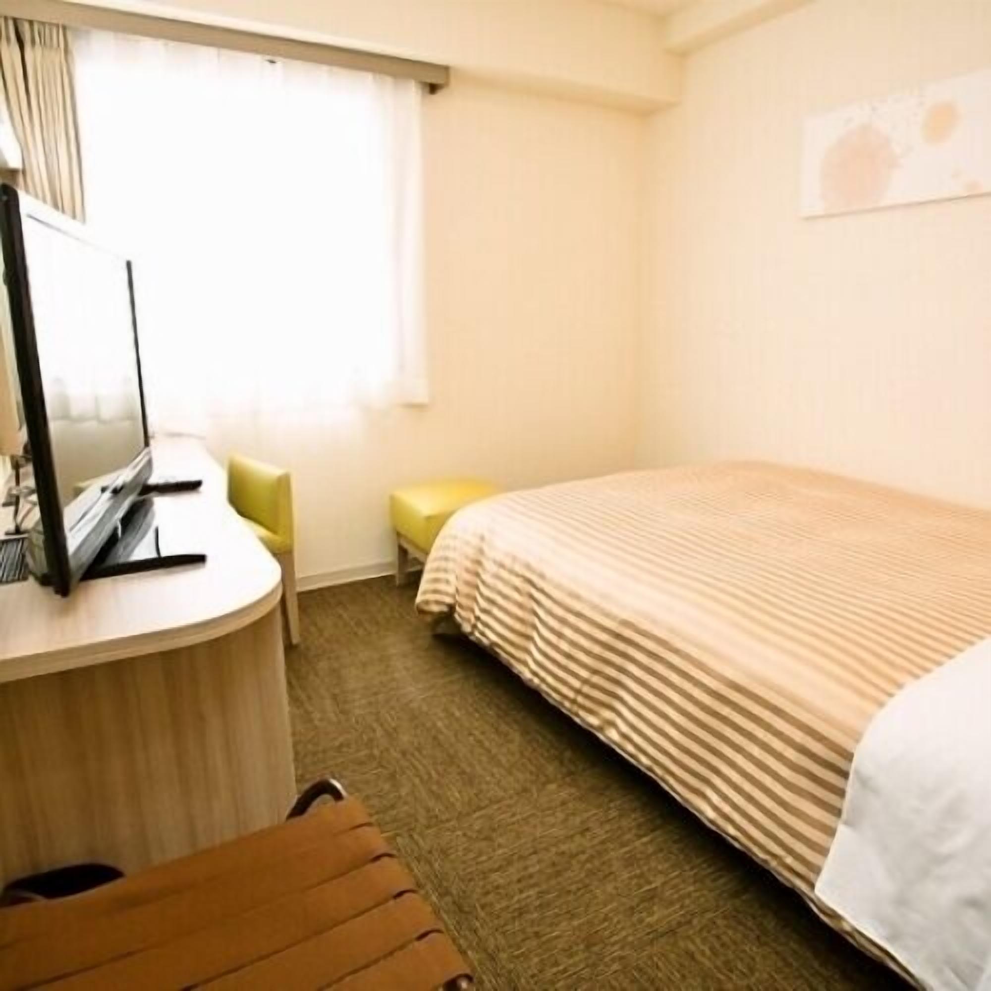Habitación de hotel con cama, escritorio con computadora, silla y ventana con cortinas.