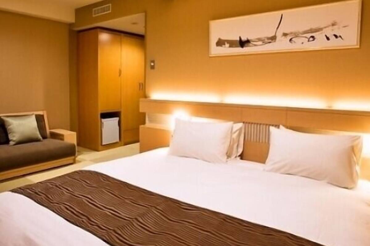 Una habitación de hotel con una cama grande, un sofá, un armario y un cuadro en la pared.