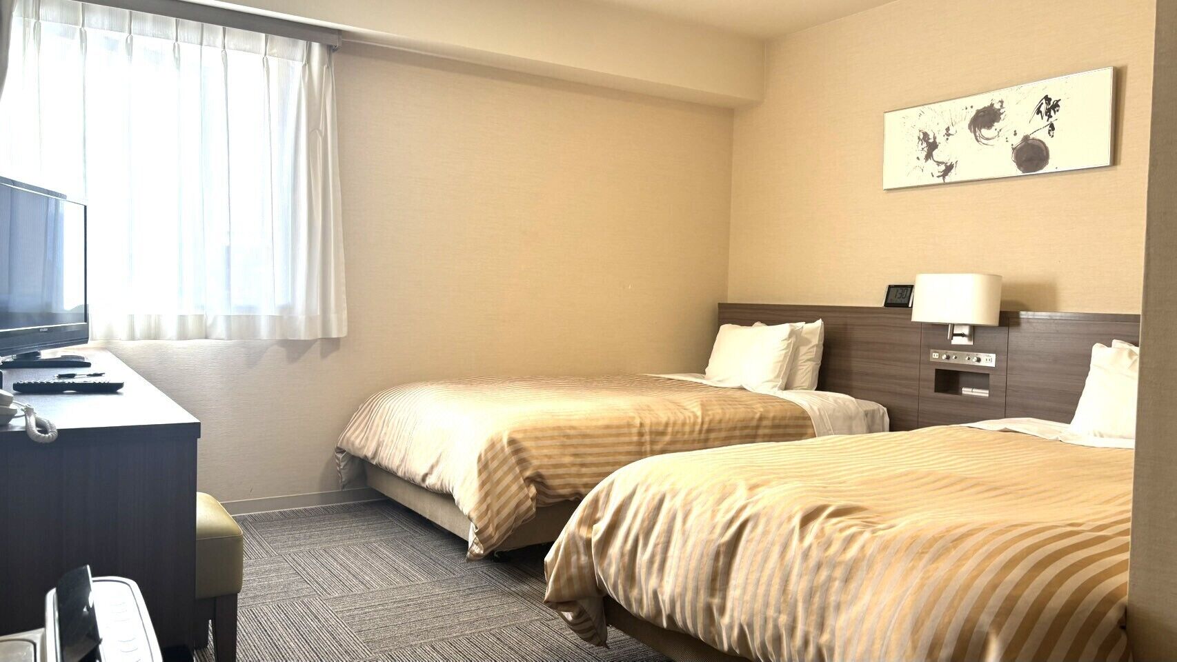 Habitación de hotel con dos camas, un escritorio con computadora, un teléfono y una obra de arte colgada en la pared.
