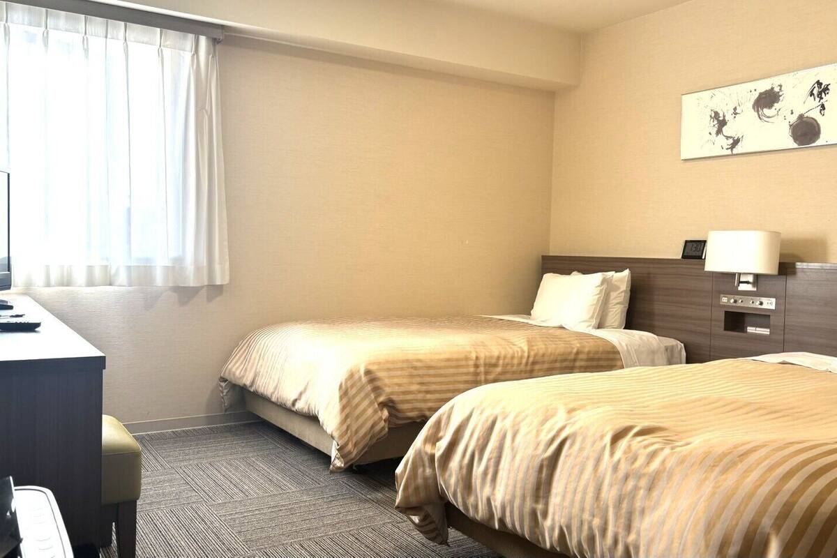 Habitación de hotel con dos camas, un escritorio con computadora, un teléfono y una obra de arte colgada en la pared.