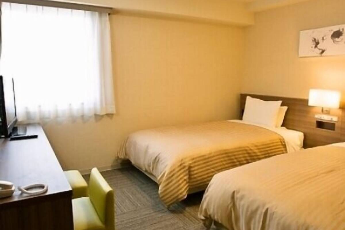 Una habitación de hotel con dos camas, un escritorio, una silla y una ventana con cortinas.