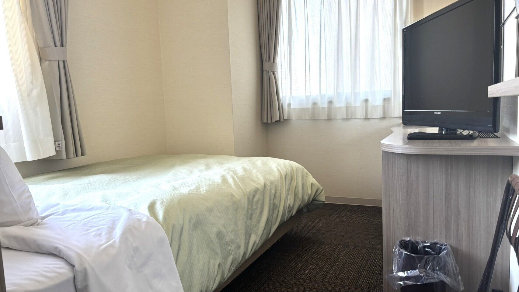 Habitación de hotel con cama, televisión sobre un mueble, escritorio con teclado y un cubo de basura.