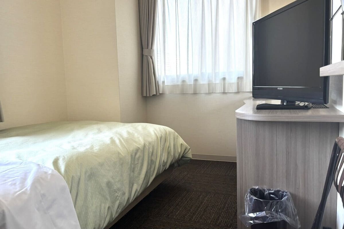 Habitación de hotel con cama, televisión sobre un mueble, escritorio con teclado y un cubo de basura.