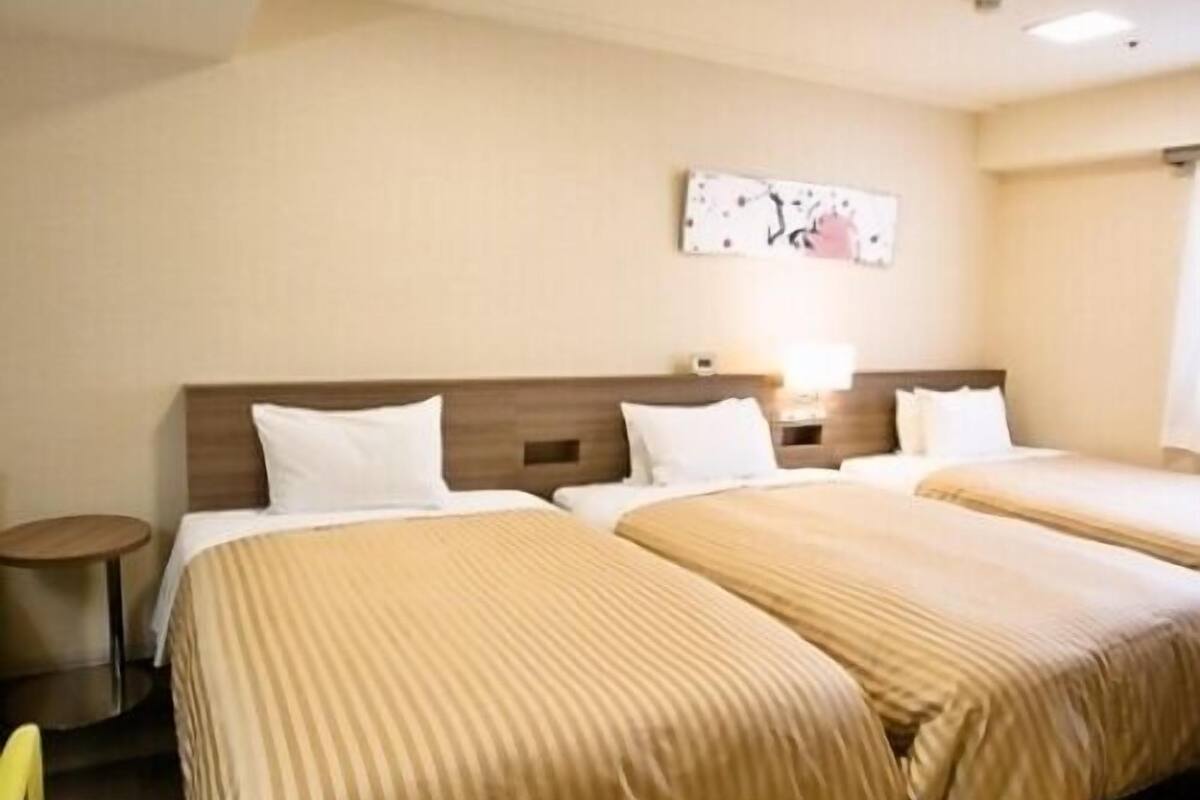 Una habitación de hotel con dos camas, una mesita redonda y un cuadro en la pared.