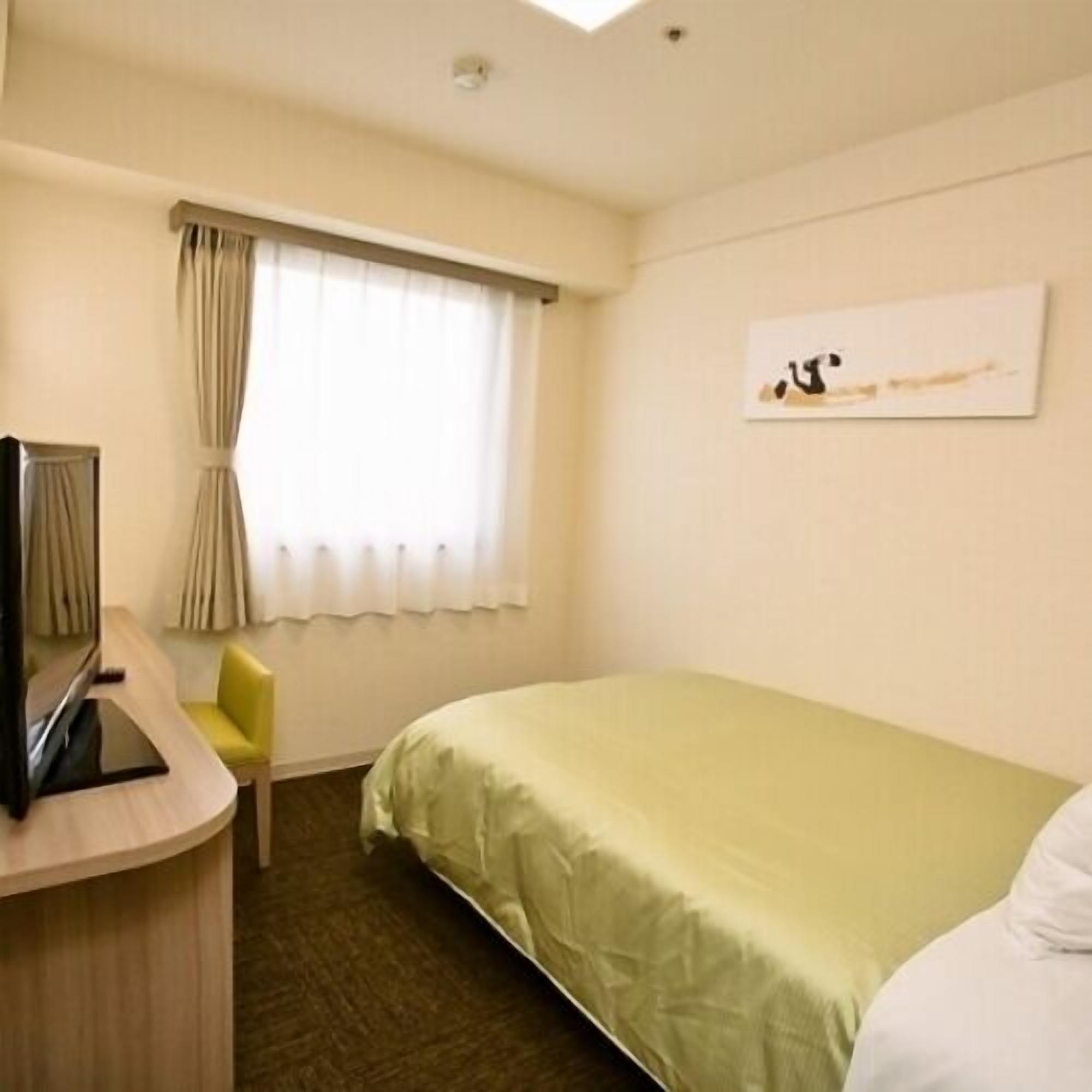 Habitación de hotel con cama, escritorio y silla, ventana con cortinas y una obra de arte en la pared.