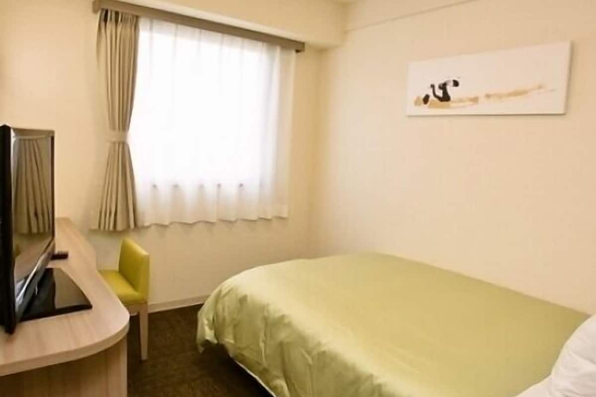 Habitación de hotel con cama, escritorio y silla, ventana con cortinas y una obra de arte en la pared.