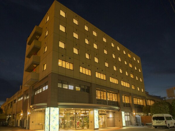 A multi-story hotel with a modern design, featuring a ground-level entrance with glass doors and a visible reception area. - Spaland Hotel Naito (Fuefuki)