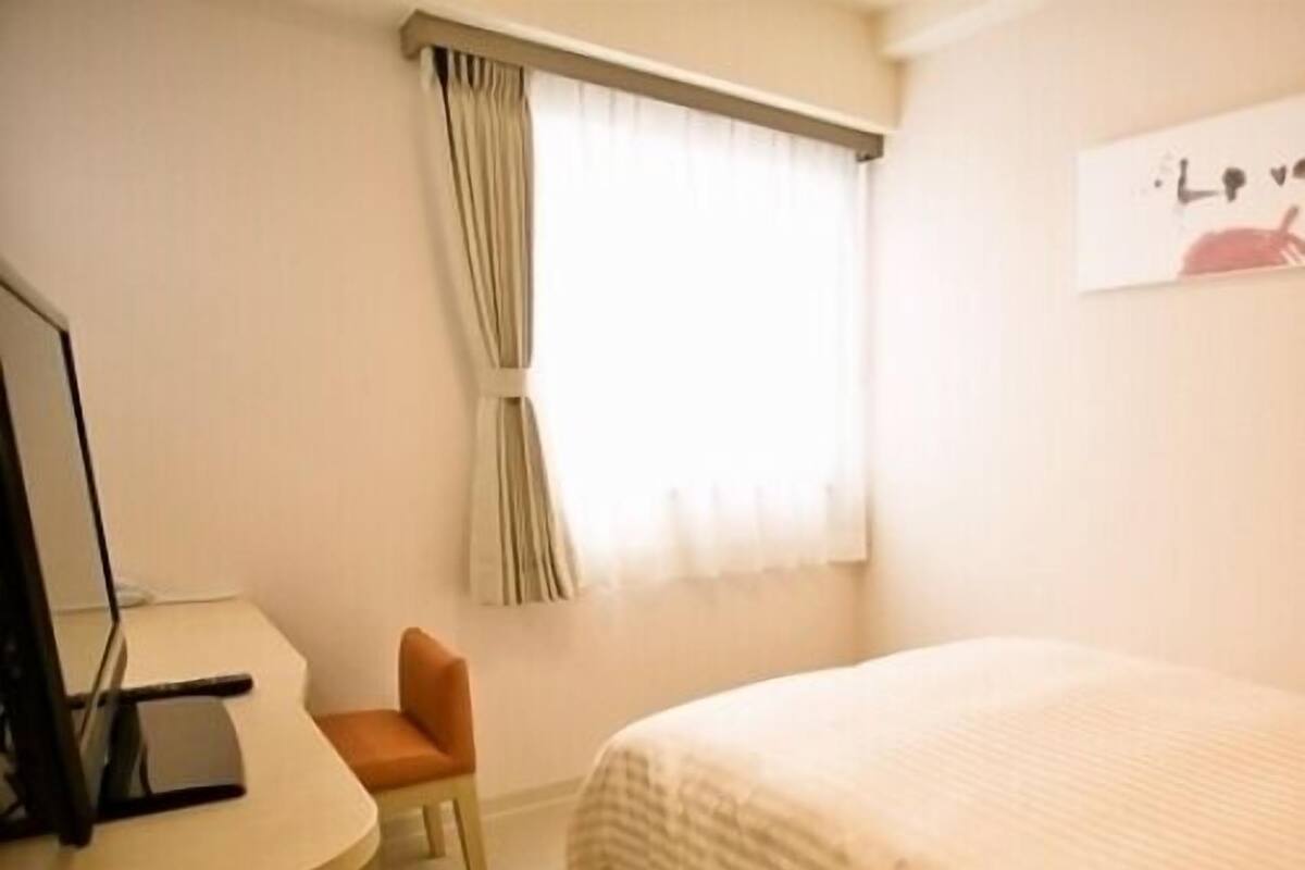 Una habitación de hotel con una cama, un escritorio, una silla y una ventana con cortinas.
