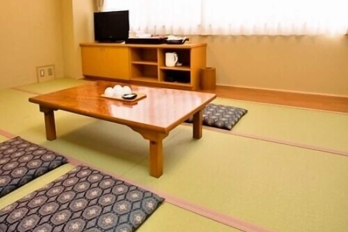 Una habitación con suelo de tatami, una mesa baja con una bandeja de objetos, un televisor sobre un mueble y una ventana con cortinas.