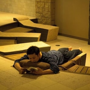 A person lying on a uniquely shaped bed in a room with a stone wall.