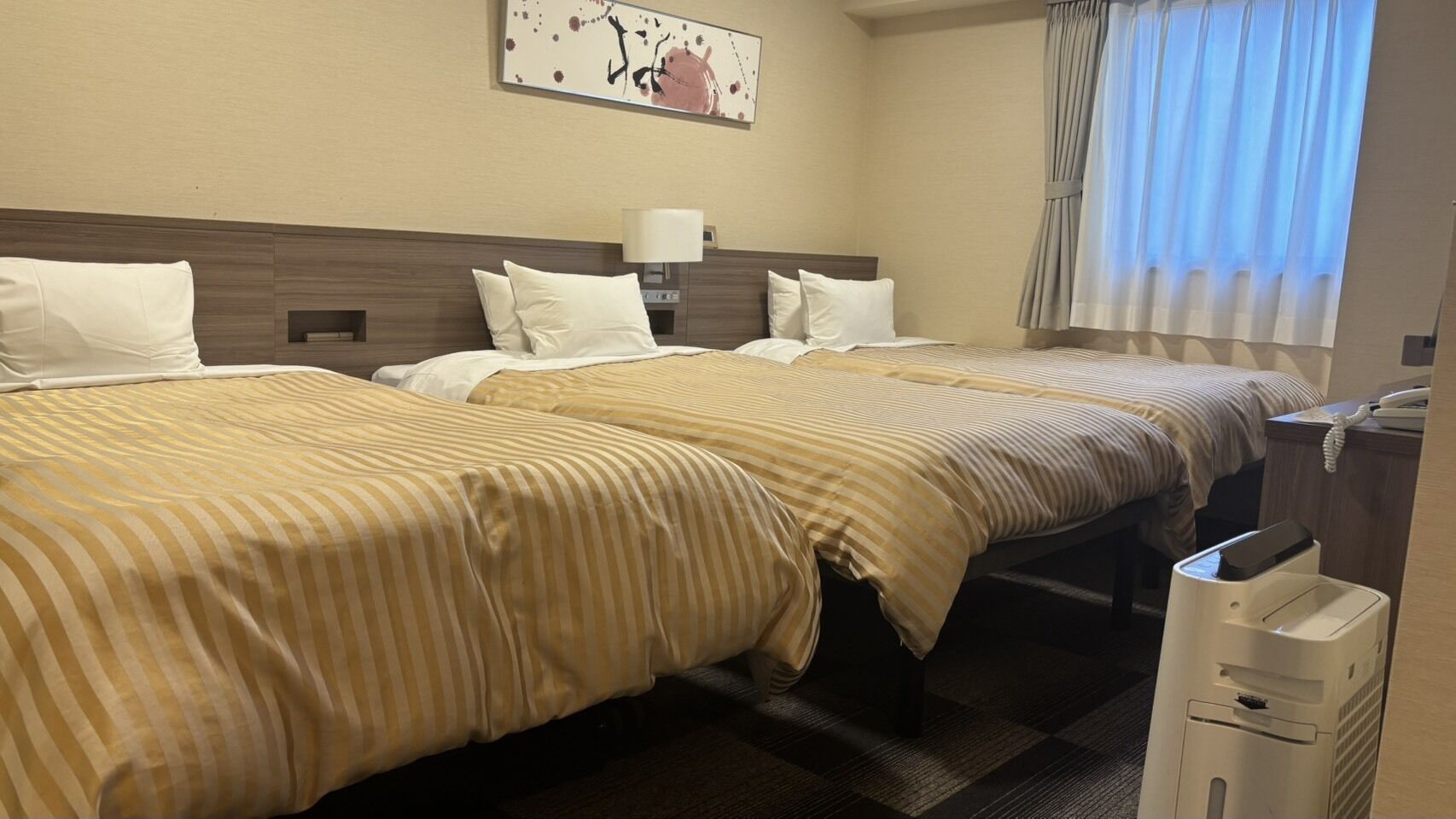 Habitación de hotel con dos camas, una mesita de noche, una lámpara, un teléfono y un cesto de basura.