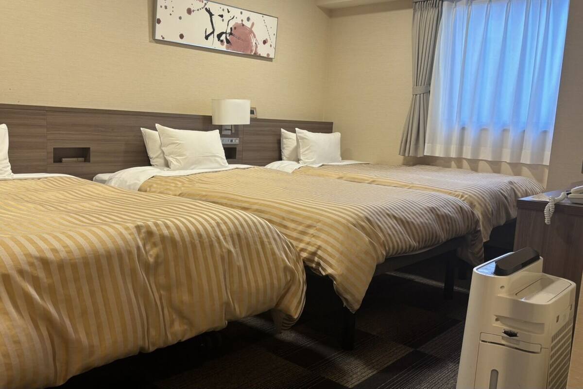 Habitación de hotel con dos camas, una mesita de noche, una lámpara, un teléfono y un cesto de basura.