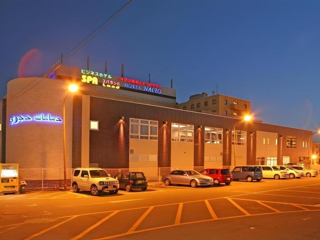 A hotel with a visible entrance, multiple parking spaces, and a clear sky.
