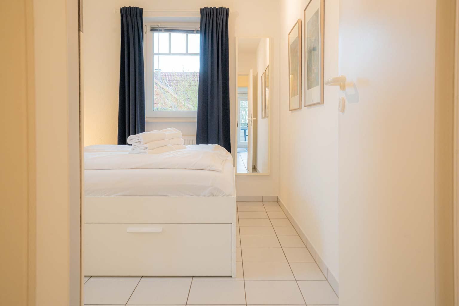 A hotel room with a bed, a window with curtains, a mirror, and framed pictures on the wall.