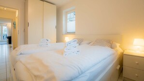 A hotel room with a large bed, a wardrobe, a bedside table with a lamp, and a window with blinds. - Apartment 6 "Schröder" (ID 045) - Haus Zum Böhler Strand 10 (Sankt Peter-Ording)
