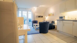 A modern kitchen with white cabinets, a microwave, and a dining area with a table and chairs. - Apartment 6 "Schröder" (ID 045) - Haus Zum Böhler Strand 10 (Sankt Peter-Ording)