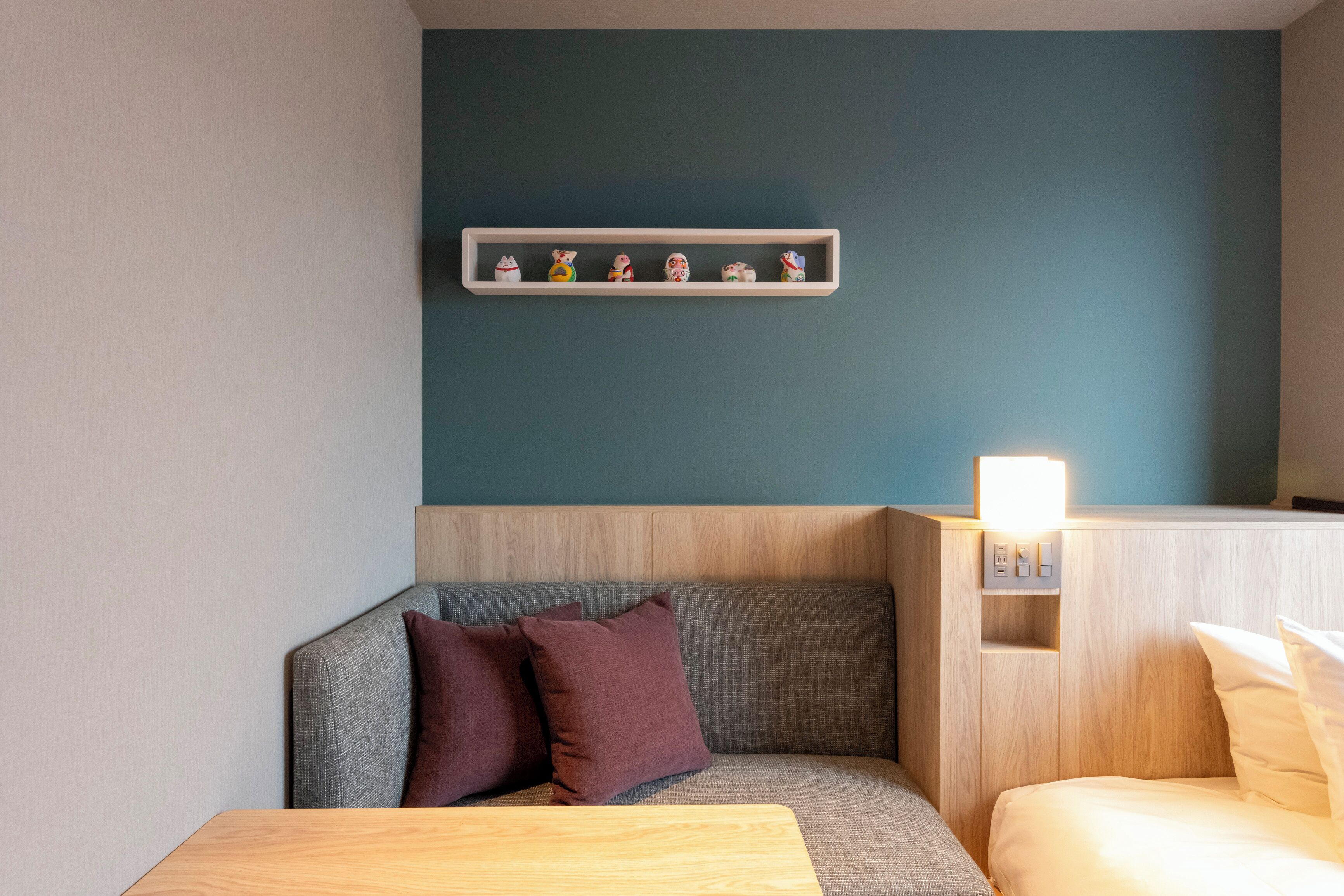 Une chambre d’hôtel moderne avec un canapé gris, une table d’appoint en bois et une étagère ornée d’objets décoratifs.