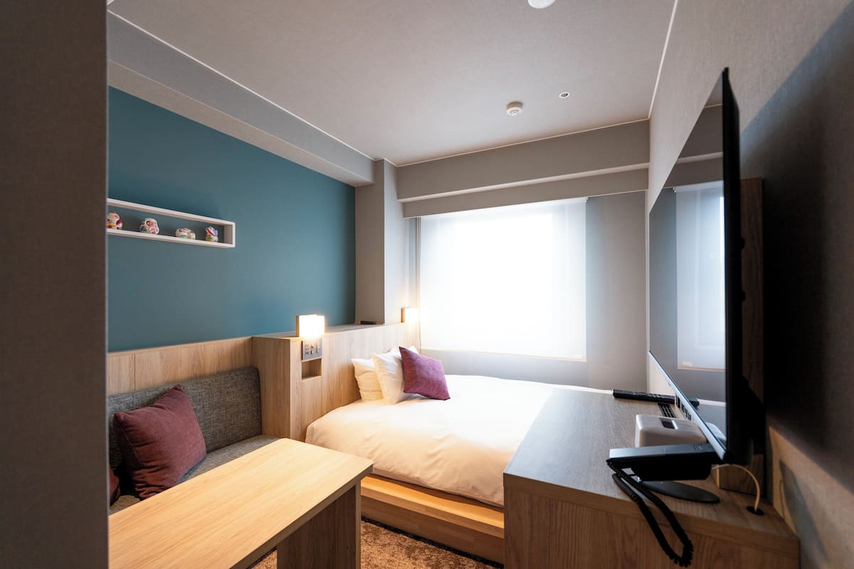 Una habitación de hotel moderna con cama, escritorio, sofá, televisor y ventana con luz natural.