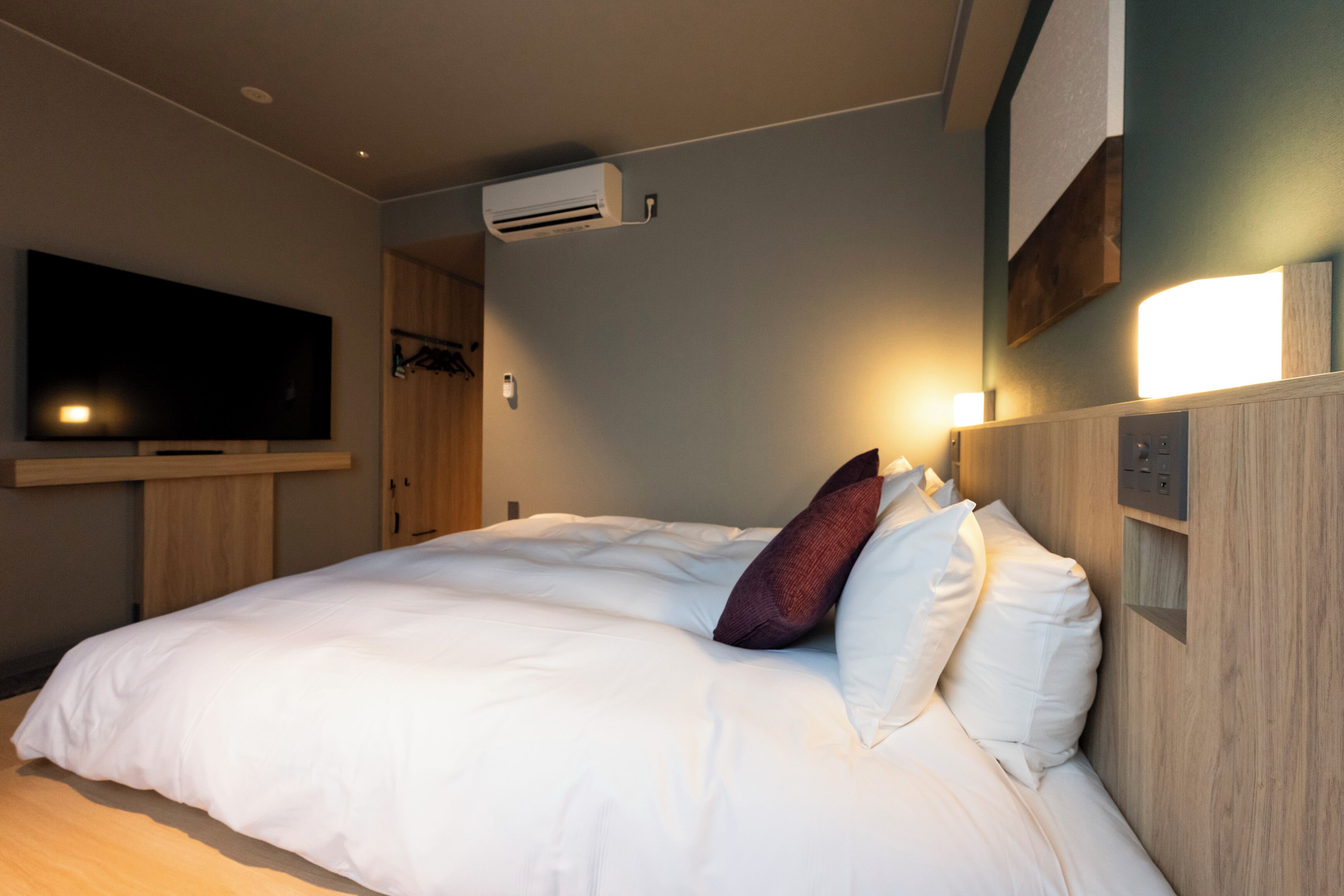 A modern hotel room with a large bed, a flat-screen TV mounted on the wall, and a wooden headboard.