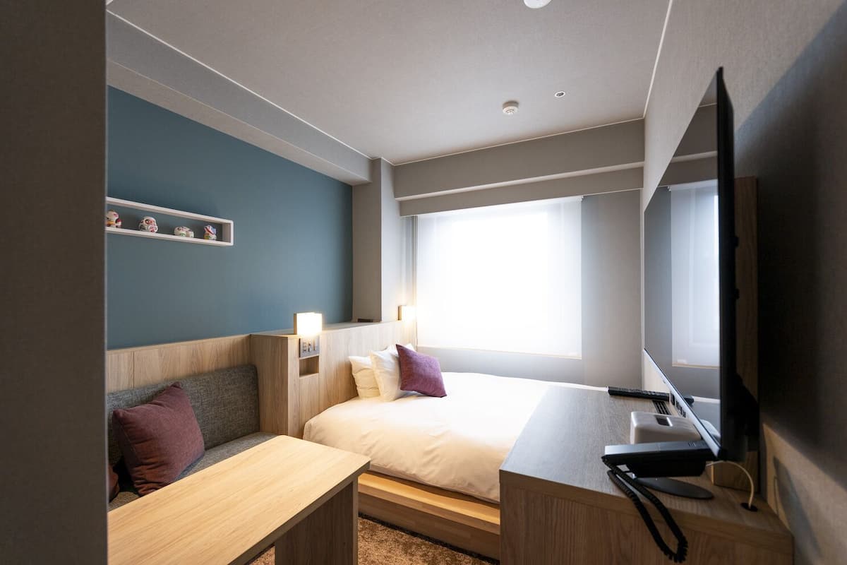 Una habitación de hotel con cama, escritorio, televisor y ventana.