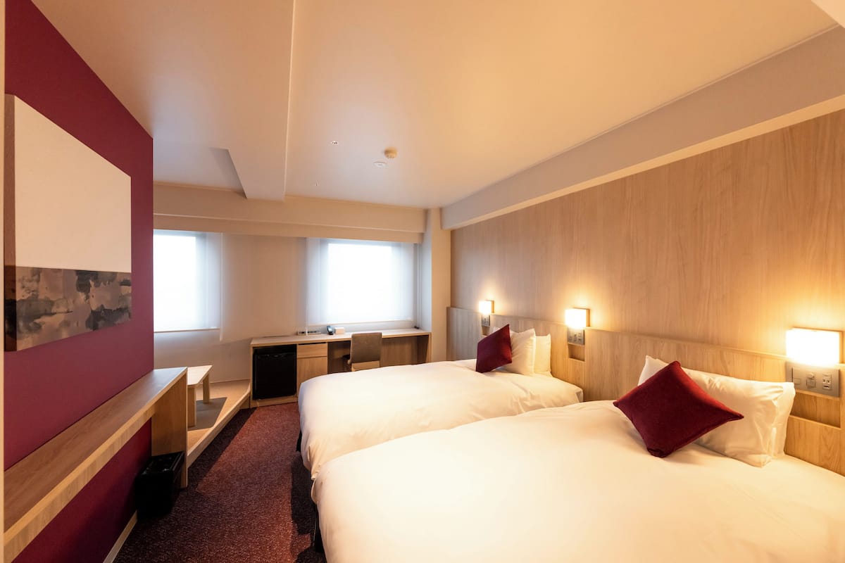 Una habitación de hotel con dos camas, un escritorio, una silla y una ventana.