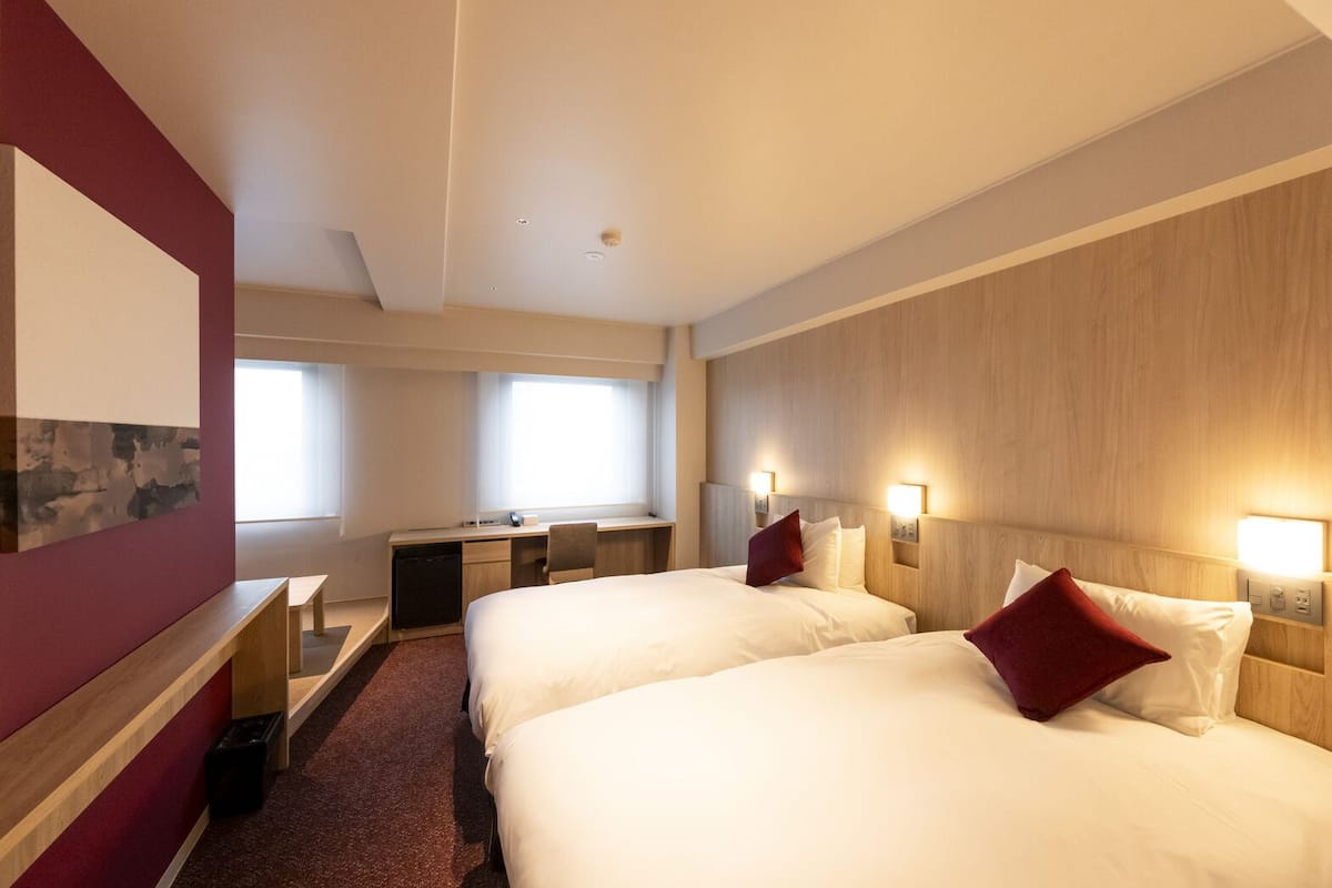 Habitación de hotel con dos camas, un escritorio y un ventanal grande.