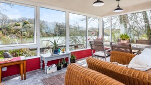 A sunroom with large windows, wicker furniture, and potted plants. - Tresowes Green Cottage (Helston)