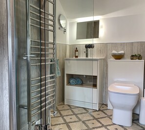 Un baño con cabina de ducha de vidrio, inodoro, lavabo con espejo y repisa con toallas.