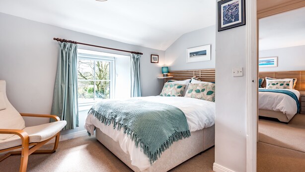 A bedroom with a bed, a chair, a window with curtains, and a picture on the wall. - Tresowes Green Cottage (Helston)